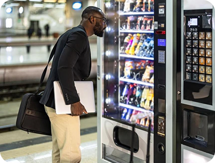 A man with a laptop examining a vending machine indoors.